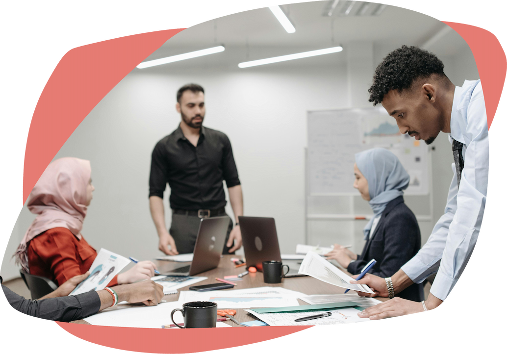 A group of four people meeting around a table with a laptop and notepads A group of four people meeting around a table with a laptop and notepads