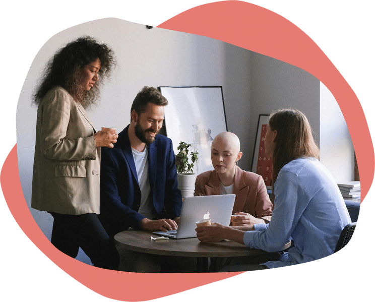 A group of four people working tigether at a table with a laptop and hot drinks
