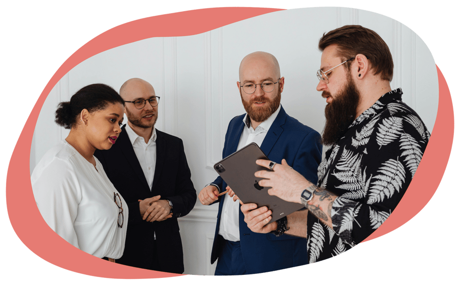 Four people standing in a meeting room looking at a tablet Four people standing in a meeting room looking at a tablet