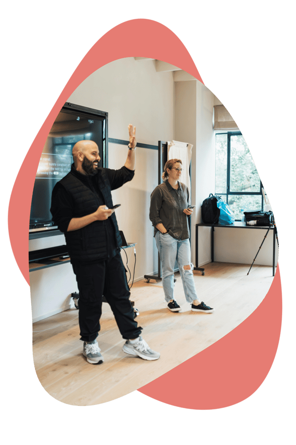 Two people standing at the front of a room delivering a session, one speaking while the other stands nearby. Two people standing at the front of a room delivering a session, one speaking while the other stands nearby.