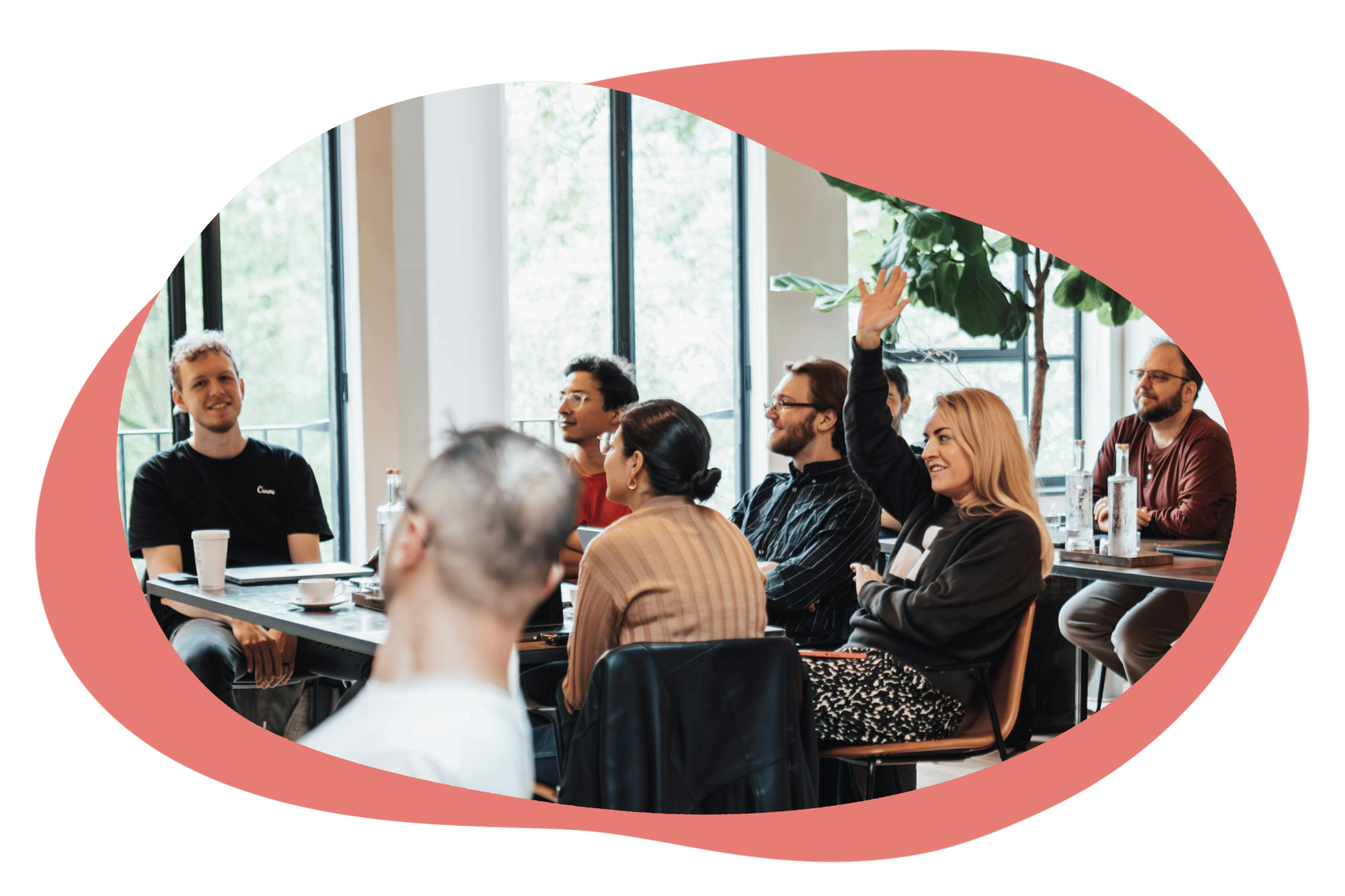 A diverse group of people sitting at a table during a training session. One person has their hand raised.