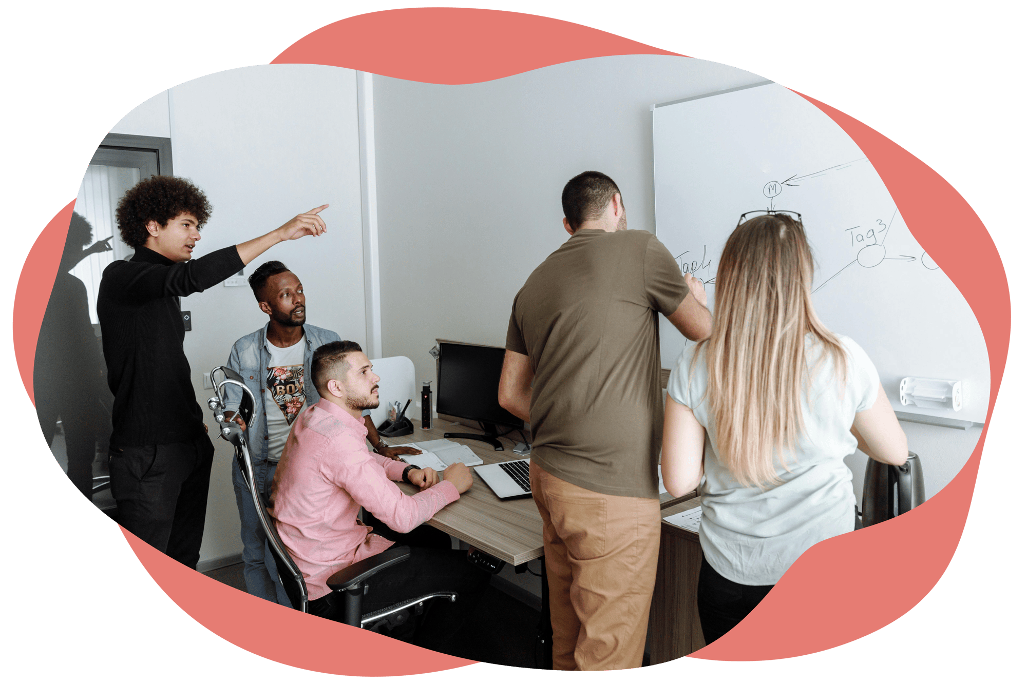 A group of people working together around a desk, with two team members writing on a whiteboard while others look on and discuss ideas.
